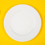 Aerial view of a white plate and silverware on a yellow background