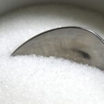 Aerial image of a silver spoon dipping into white sugar, which can cause cavities