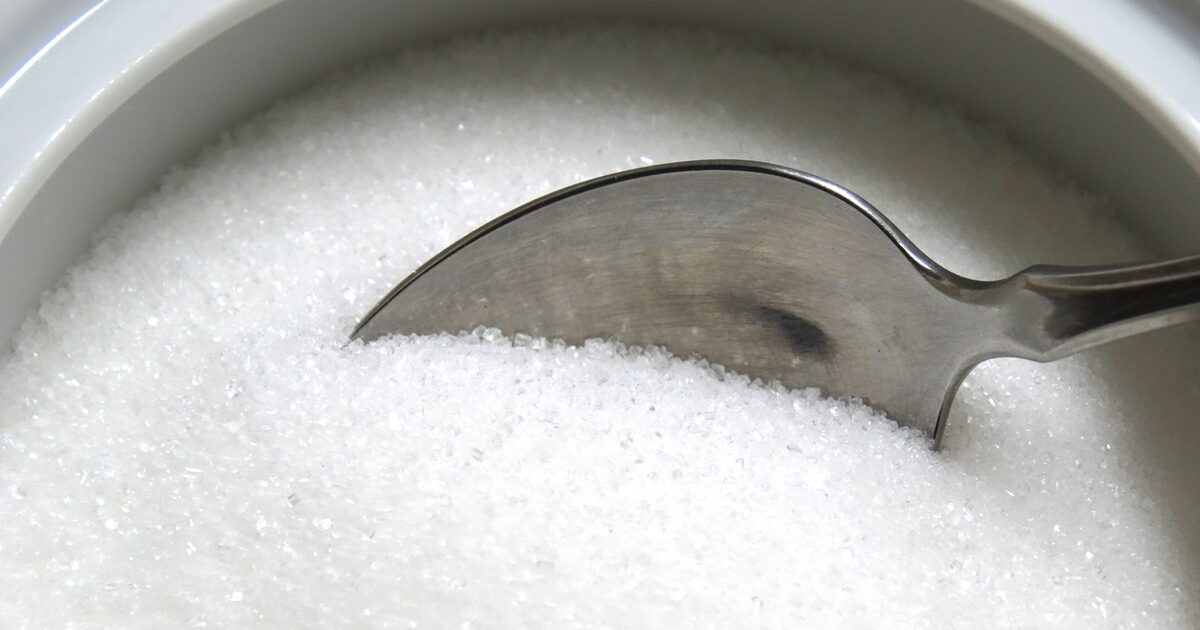 Aerial image of a silver spoon dipping into white sugar, which can cause cavities